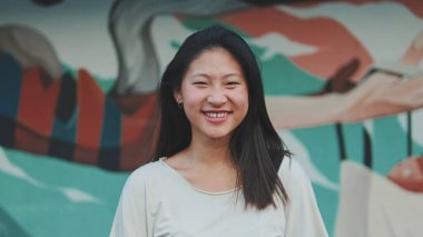 Güzel, mutlu esmer kız, günlük giysiler içinde kameraya bakıp gülüyor.