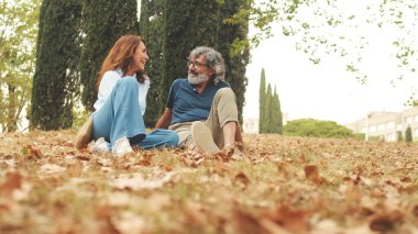 Emekli çift konuşuyor, sonbaharda parkta çimlerin üzerinde oturuyor.