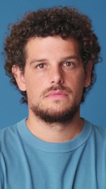 Yakından, genç adam kameraya bakıyor. Stüdyonun mavi arka planında izole edilmiş.