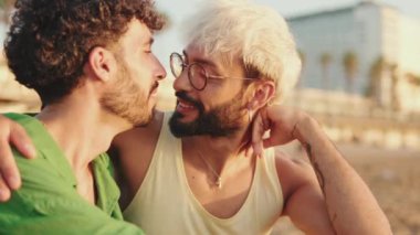 Yakın plan, homoseksüel çift sahilde otururken sarılıp öpüşüyorlar.