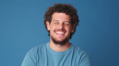 Yakından, genç adam kameraya bakıyor ve gülüyor. Stüdyonun mavi arka planında izole edilmiş.