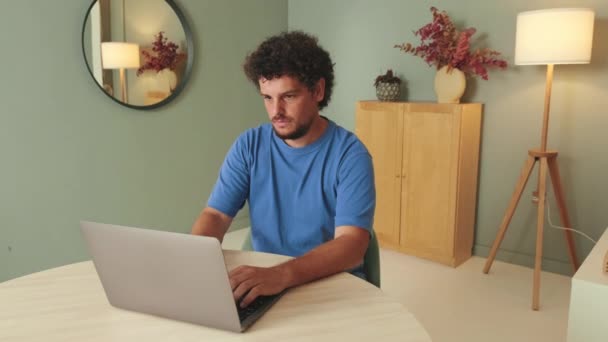 男の学生はテーブルのリビングルームに座っている間 ノートパソコンを使用します — ストック動画