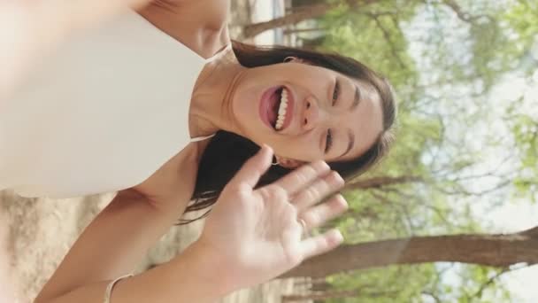 市立公園に立っている間に携帯電話からビデオ通話をする笑顔の若い女性のクローズアップ — ストック動画