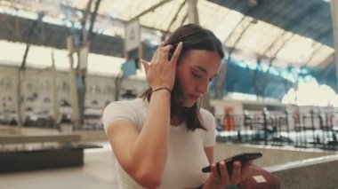 Gezgin kadın tren istasyonunda oturuyor ve akıllı telefon kullanıyor.