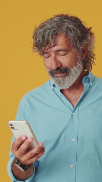 Verrassende Oudere Grijsharige Man Kijkt Naar Mobiele Telefoon Geïsoleerd Oranje — Stockvideo