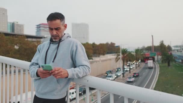Μεσήλικας Αθλητικά Χρησιμοποιεί Κινητό Ενώ Στέκεται Στη Γέφυρα — Αρχείο Βίντεο