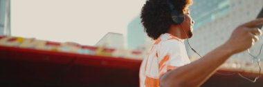 Tişört giyen, kulaklıkla müzik dinleyen ve şehir arka planında dans eden neşeli genç Afrikalı Amerikalı adamın yakın çekimi. Yaşam tarzı kavramı