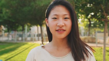 Yakından, sıradan kıyafetler giymiş güzel esmer kız kameraya bakıyor ve gülümsüyor.