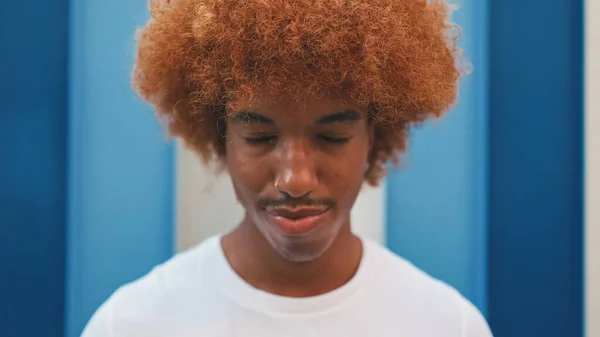 stock image Close up, guy with an African hairstyle dressed in white T-shirt posing with eyes closed on striped wall background