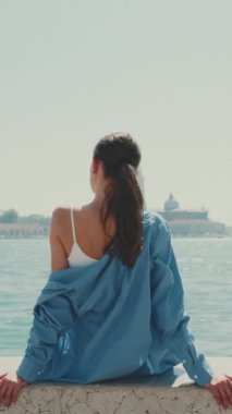 Dikey video, uzun kahverengi saçlı, mavi gömlekli güzel bir kız Venedik 'te bir sette oturuyor.