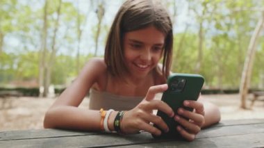 Parkta otururken cep telefonuyla video izleyen mutlu genç kız.