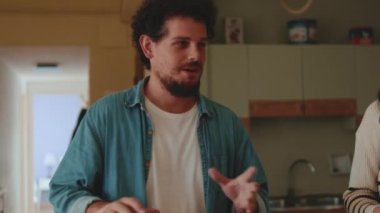 Oturma odasında konuşan ve el kol hareketi yapan adam.