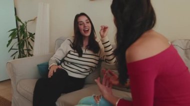 İki kız arkadaş kanepede oturmuş sohbet ediyor ve eğleniyorlar.