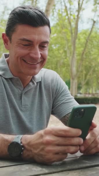 Hombre Mediana Edad Desplaza Teléfono Móvil Mientras Está Sentado Banco — Vídeos de Stock