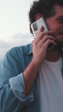 Balkonda dururken akıllı telefondan konuşan mutlu genç adam.