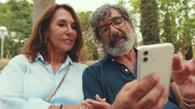 Olgun bir çift parkta otururken konuşuyor ve cep telefonu kullanıyor.