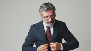 Orta yaşlı iş adamı kravatını düzeltiyor, gri arka planda izole edilmiş.