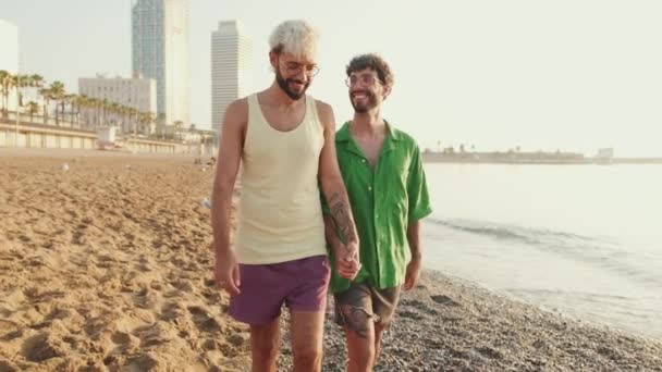 ハッピーゲイカップルは彼らの腕が交差してビーチを歩いています — ストック動画