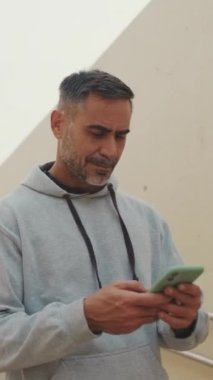 Spor kıyafetleri içinde orta yaşlı bir adam eğitimden sonra cep telefonuna SMS mesajı yazıyor.