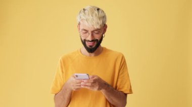 Elinde telefon olan gülümseyen bir adam. Stüdyoda sarı arka planda izole edilmiş bir model alanı var.