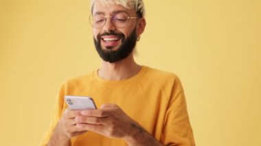 Yakın plan, erkekler SMS okurken güler, cep telefonundan video izlerler, sarı arka planda izole olurlar.