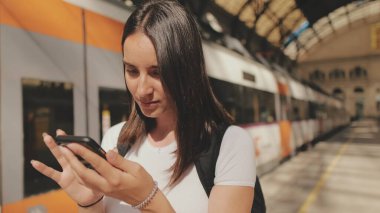 Güzel kız gezgin tren istasyonunun peronunda dururken cep telefonu kullanıyor.