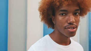 Yakından, beyaz tişörtlü Afrikalı bir adam çizgili arka plandaki kameraya bakıyor.