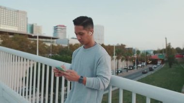 Telsiz kulaklıklı genç adam, köprüde duruyor ve cep telefonu kullanıyor.