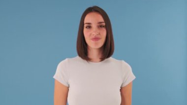 Kameraya bakan şaşırmış bir kadın stüdyoda mavi arka planda el çırpıyor.