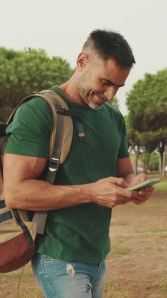 Hombre Mediana Edad Camina Por Parque Sosteniendo Teléfono Inteligente — Vídeos de Stock