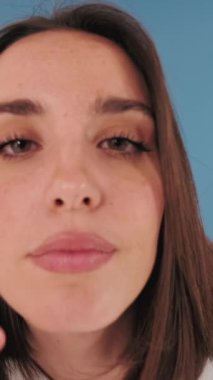 Yakın plan, kameraya bakan bir kadın stüdyodaki mavi arka planda izole edilmiş aynaya bakıyor.