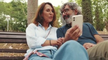 Yaşlı çift parkta otururken cep telefonu kullanırken iyi eğlenceler.