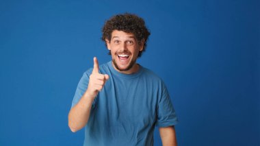 Mavi tişörtlü, kıvırcık saçlı memnun adam zor bir seçim düşünüyor. Kafasında bir plan kuruyor. Stüdyoda mavi arka planda izole edilmiş bir planı var.