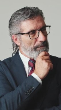 Orta yaşlı iş adamının elleri çenesini destekliyor, gri arka planda izole edilmiş.