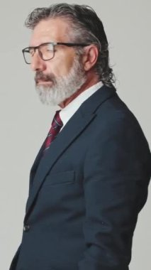 Orta yaşlı işadamı kollarını kavuşturup gri arka planda izole bir şekilde kameraya bakar.