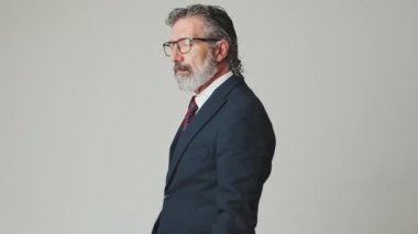 Orta yaşlı işadamı kollarını kavuşturup gri arka planda izole bir şekilde kameraya bakar.