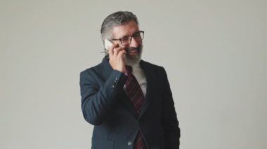 Akıllı telefondan konuşan mutlu iş adamı, gri arka planda izole edilmiş.