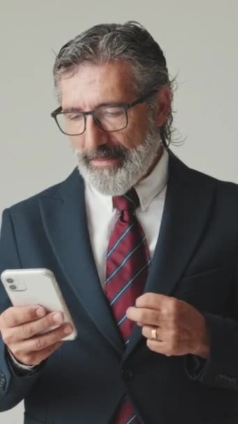 グレーの背景で孤立した良いニュースを受け取るスマートフォンを見ている幸せなビジネスマン — ストック動画