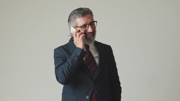 グレーの背景で孤立したスマートフォンで話す幸せなビジネスマン — ストック動画