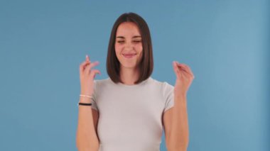 Genç bir kadın dilek diliyor. Stüdyonun mavi arka planında izole edilmiş kameraya bakıyor.