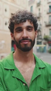 Sakallı, yeşil tişörtlü yakışıklı esmer adam kameraya bakarken kollarını kavuşturuyor.