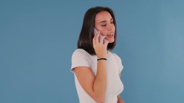 好消息 年轻的女人 在蓝色背景的孤立无援的手机上说话时很惊讶 — 图库视频影像