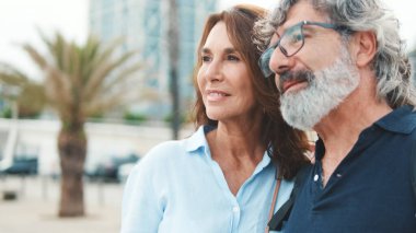 Yaşlı bir çiftin setin kenarında durup birbirlerine gülümseyerek baktıkları yakın plan.