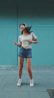 Kulaklık takmış, müzik dinleyen ve mavi duvarda dans eden mutlu, güzel esmer kız.