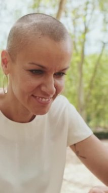 Güzel, mutlu bir kadın, park bankında otururken telefonunu kaydırıyor. Kamera uzaklaşıyor.