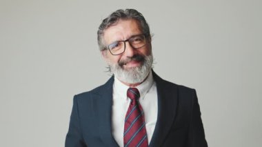 Orta yaşlı işadamı, gri arka planda izole edilmiş kameraya bakarak iyi niyet gösterisi yapıyor.