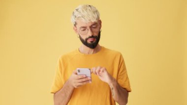 Elinde telefon olan adam sarı arka planda izole edilmiş alışverişleri seçer, seçer.