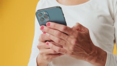 Stüdyoda sarı arka planda izole edilmiş cep telefonu kullanan genç kadınların yakın çekimleri