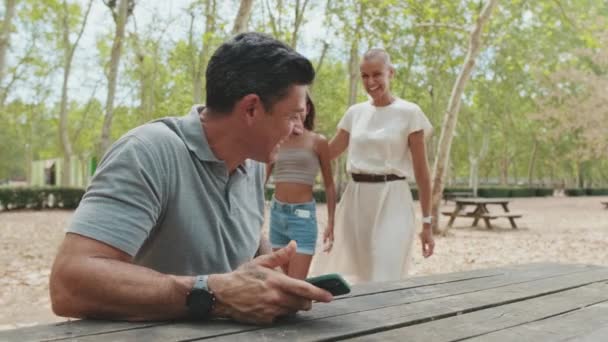 Άντρας Κρατώντας Τηλέφωνο Ενώ Κάθεται Στο Παγκάκι Του Πάρκου Ευτυχής — Αρχείο Βίντεο