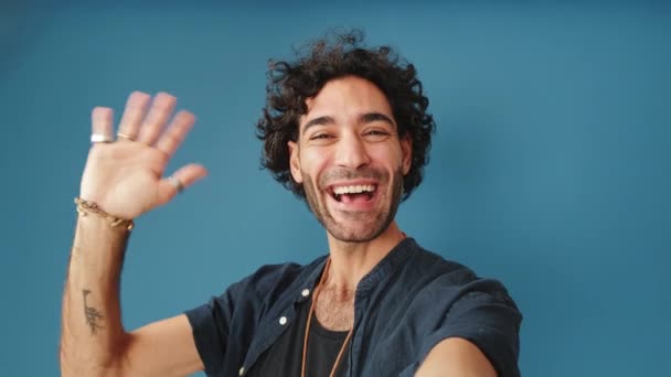 Χαμογελώντας Άνθρωπος Κοιτάζοντας Κάμερα Κάνοντας Βιντεοκλήση Σημάδι Καλωσορίσματος Απομονώνονται Μπλε — Αρχείο Βίντεο